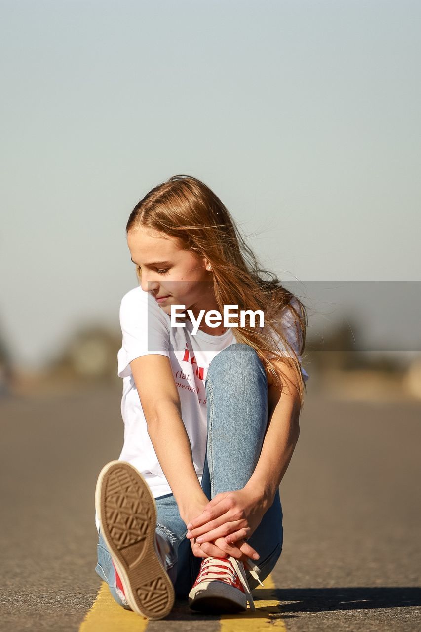 Full length of teenage girl sitting on road