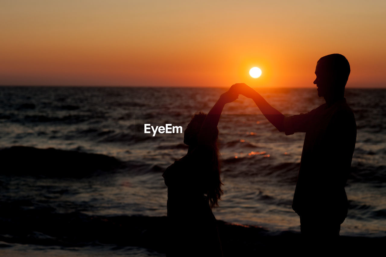 SILHOUETTE PEOPLE STANDING ON BEACH DURING SUNSET