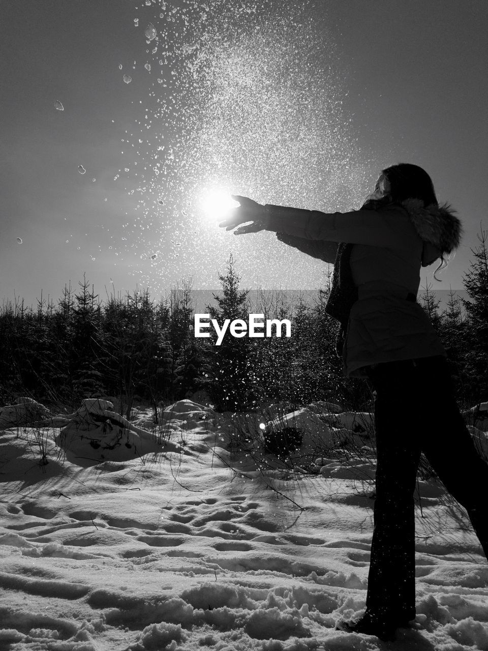 Woman throwing snow on field against sky