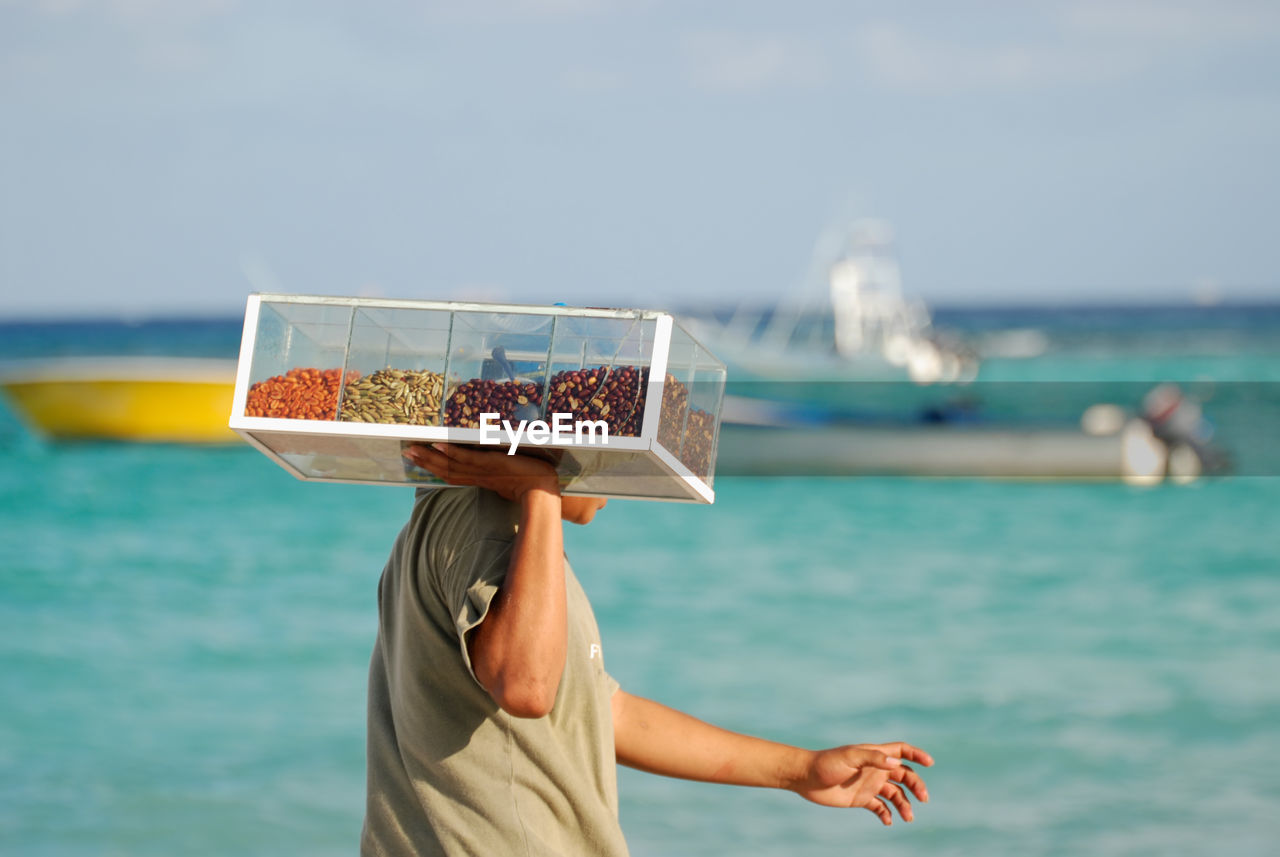 MIDSECTION OF WOMAN HOLDING UMBRELLA AGAINST SEA