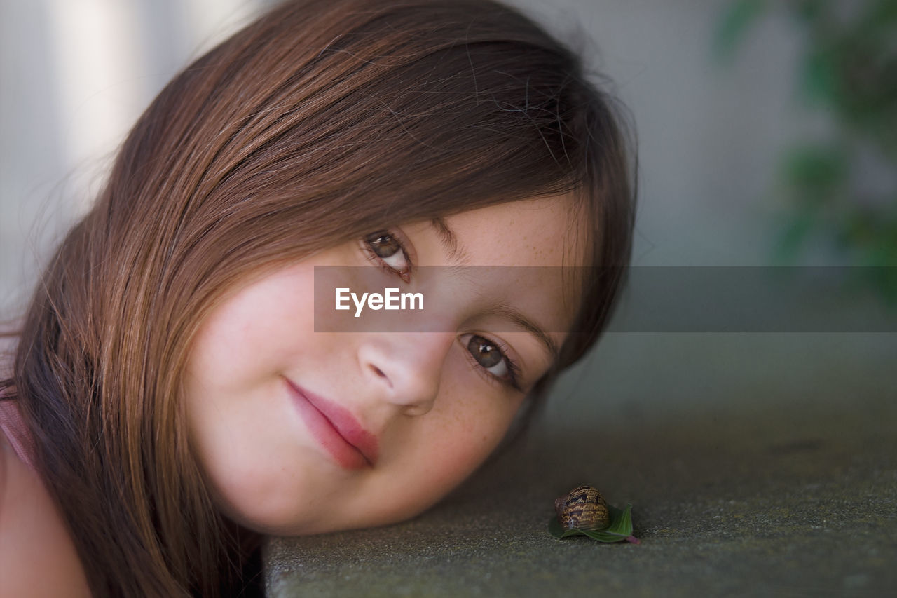 Portrait of girl leaning on retaining wall with snail