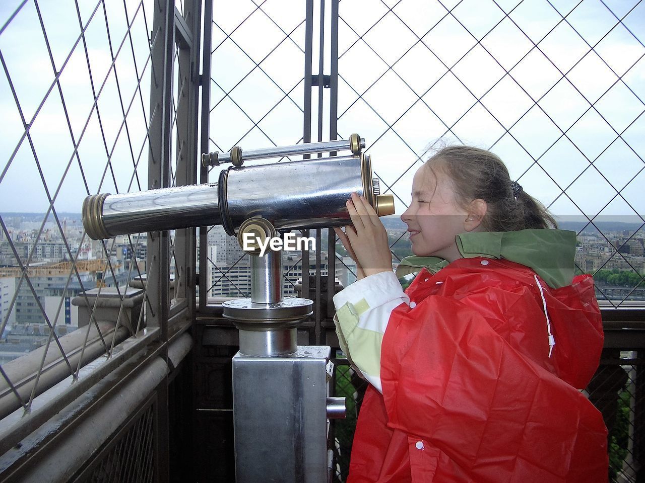 Side view of girl using hand-held telescope at eiffel tower