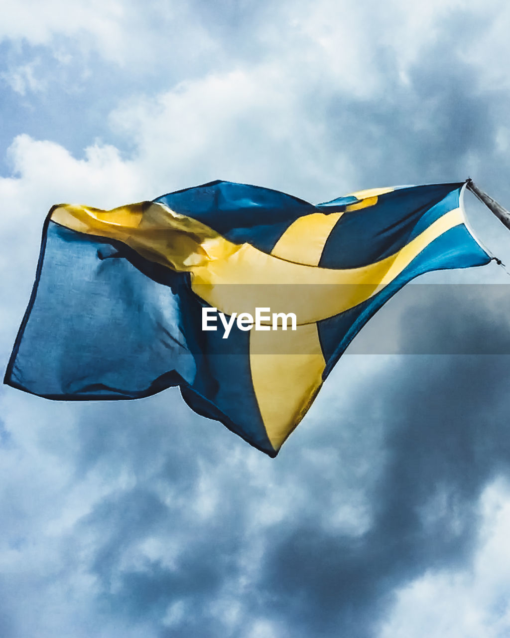 Low angle view of swedish flag against cloudy sky