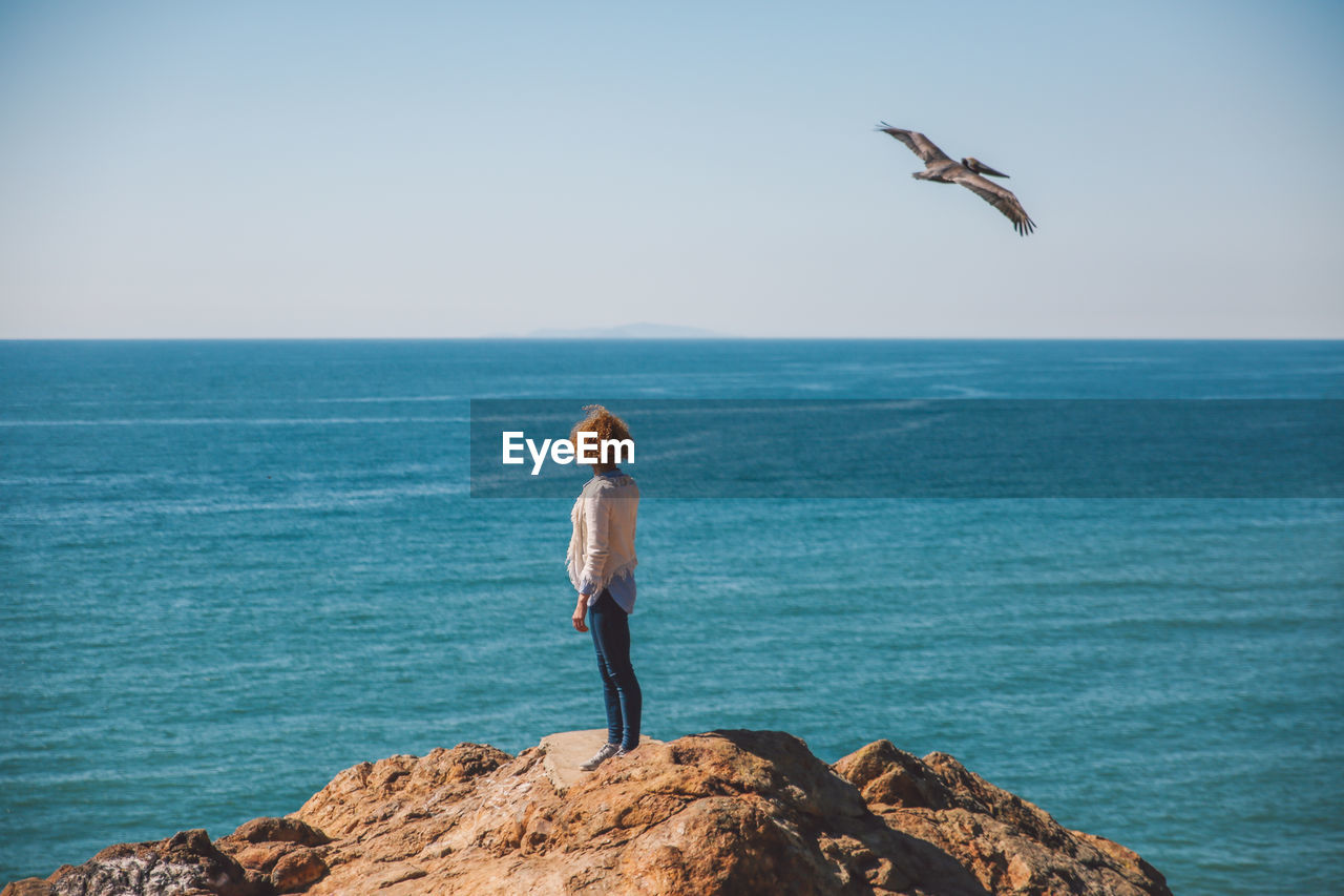 Young woman standing on rock against sea