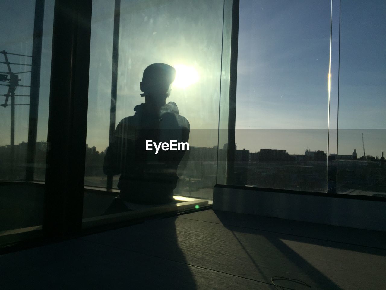 SILHOUETTE MAN STANDING BY GLASS WINDOW OF BUILDING