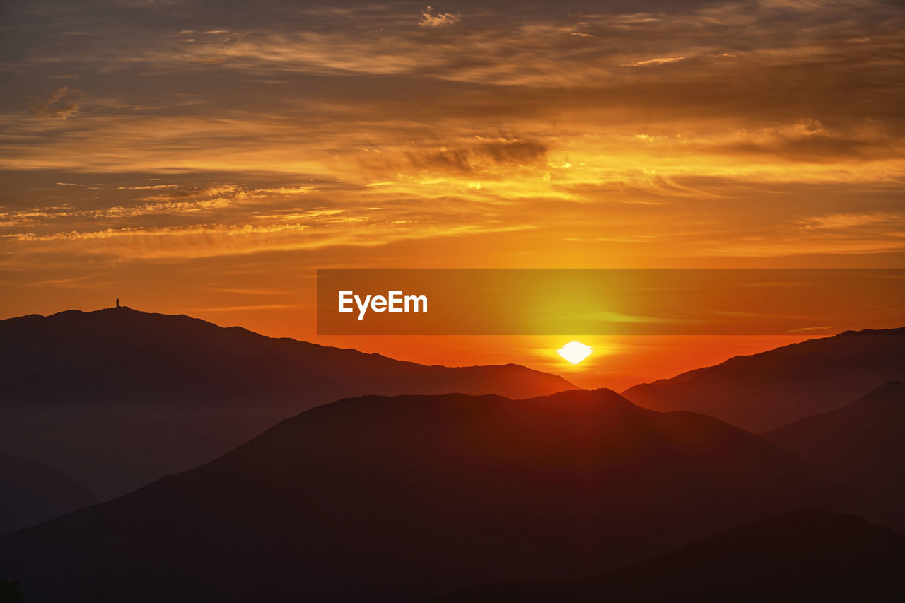 SCENIC VIEW OF SILHOUETTE MOUNTAINS AGAINST ORANGE SKY