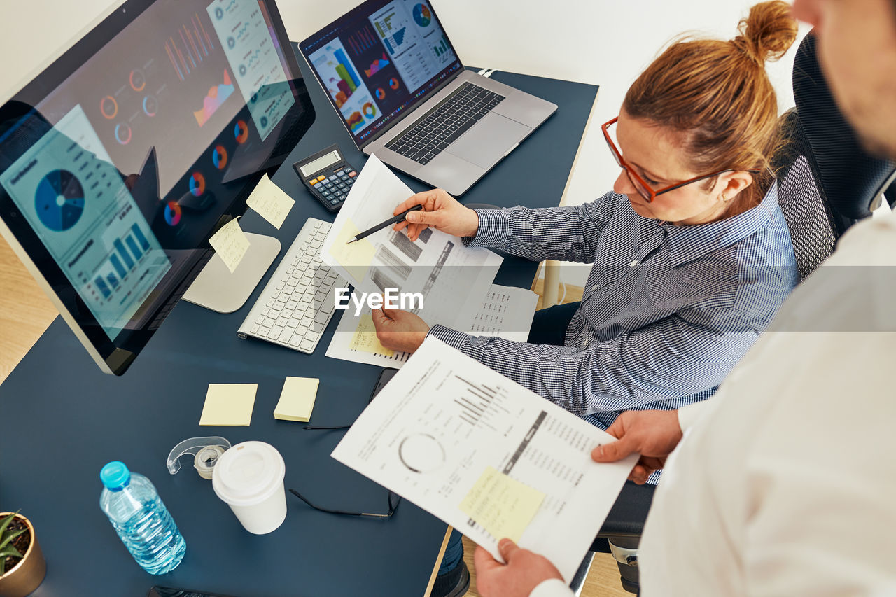 Businesswoman discussing financial data with colleague sitting at desk in office. working together