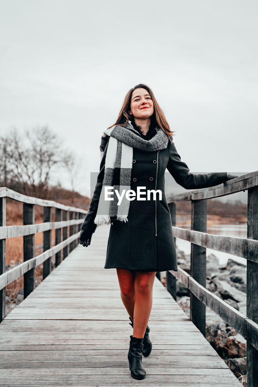 FULL LENGTH OF WOMAN STANDING ON FOOTBRIDGE IN WINTER