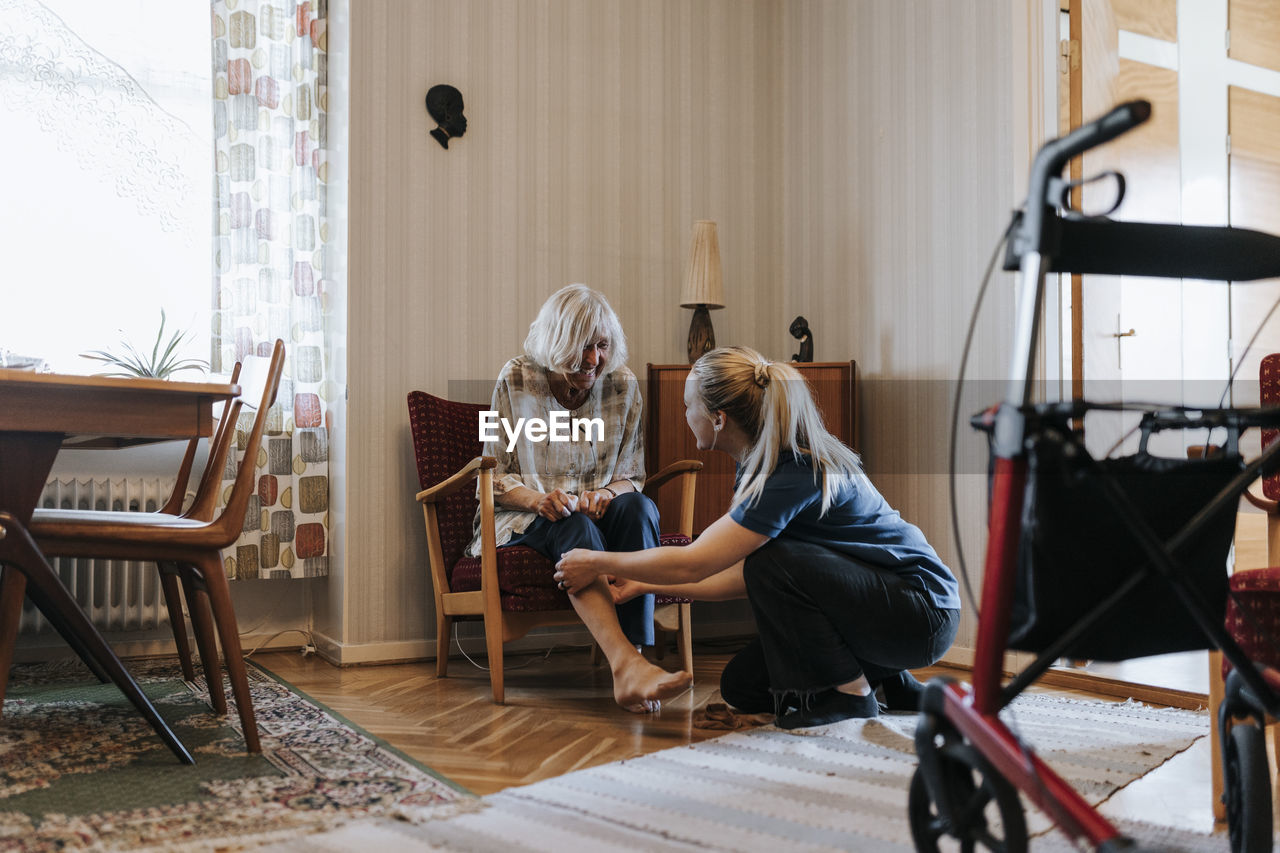 Female care assistant helping senior woman while wearing socks at home