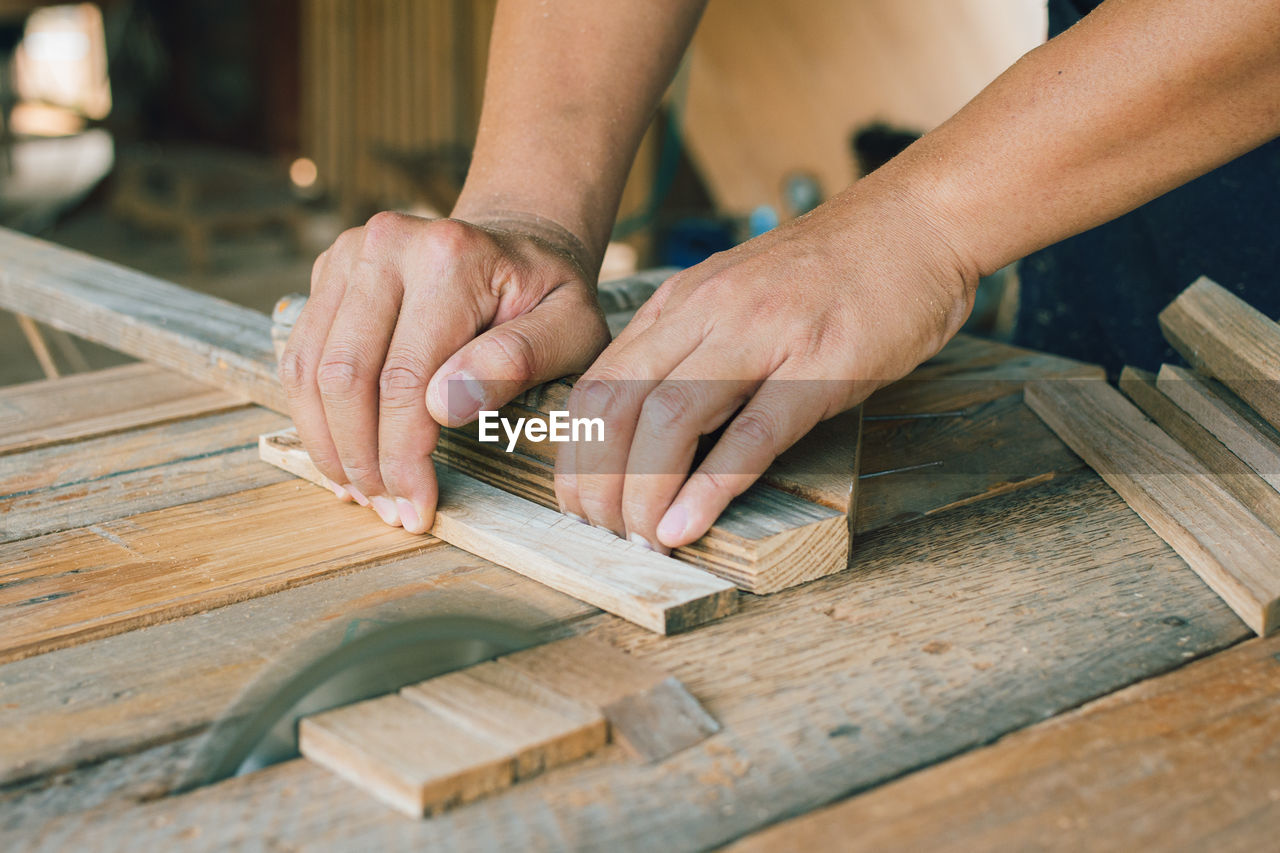 Carpenter is using a circular saw to cut wood to construct a storage box on desk  at his factory