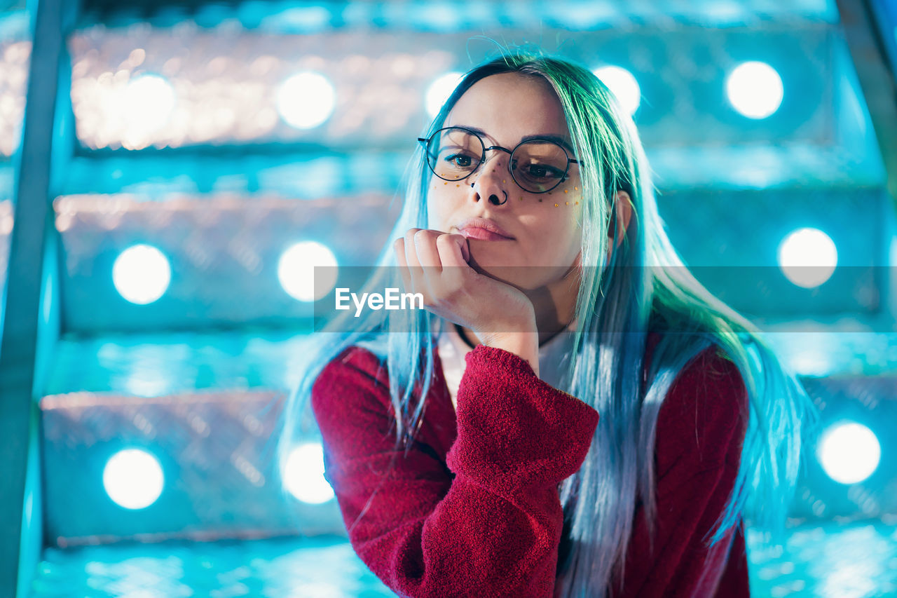 Thoughtful young woman sitting against illuminated steps