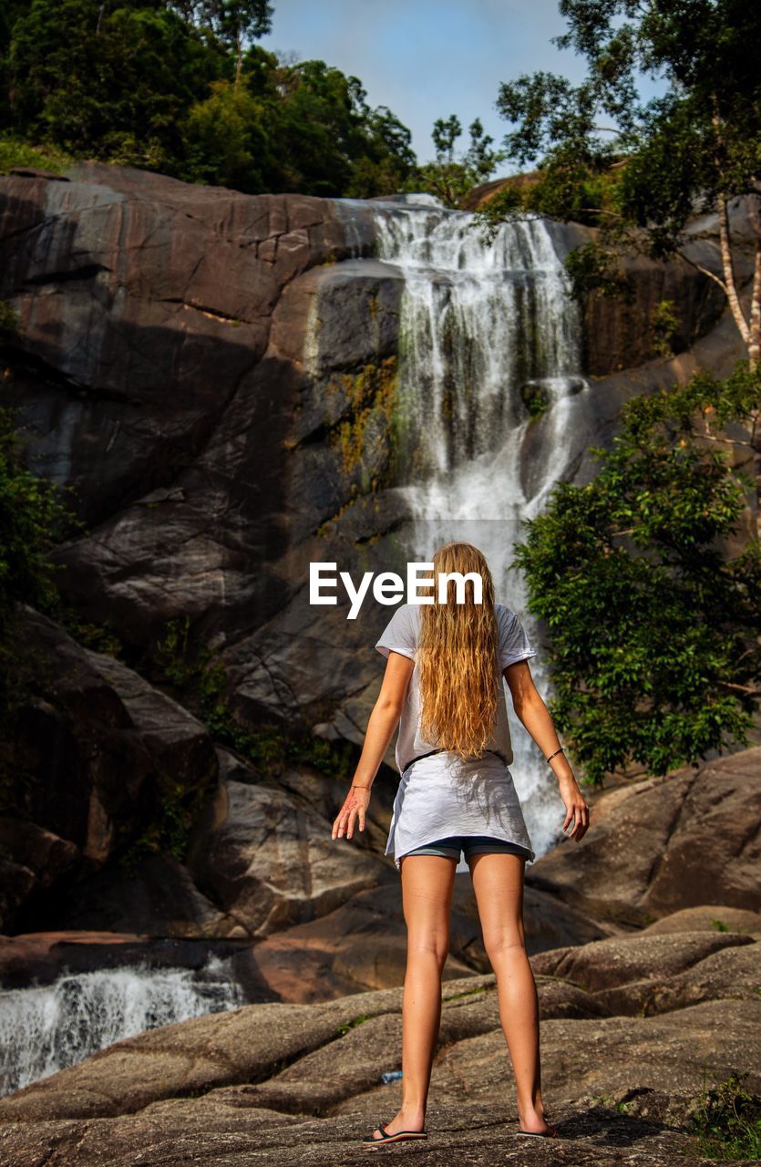 Rear view of teenage girl standing against waterfall