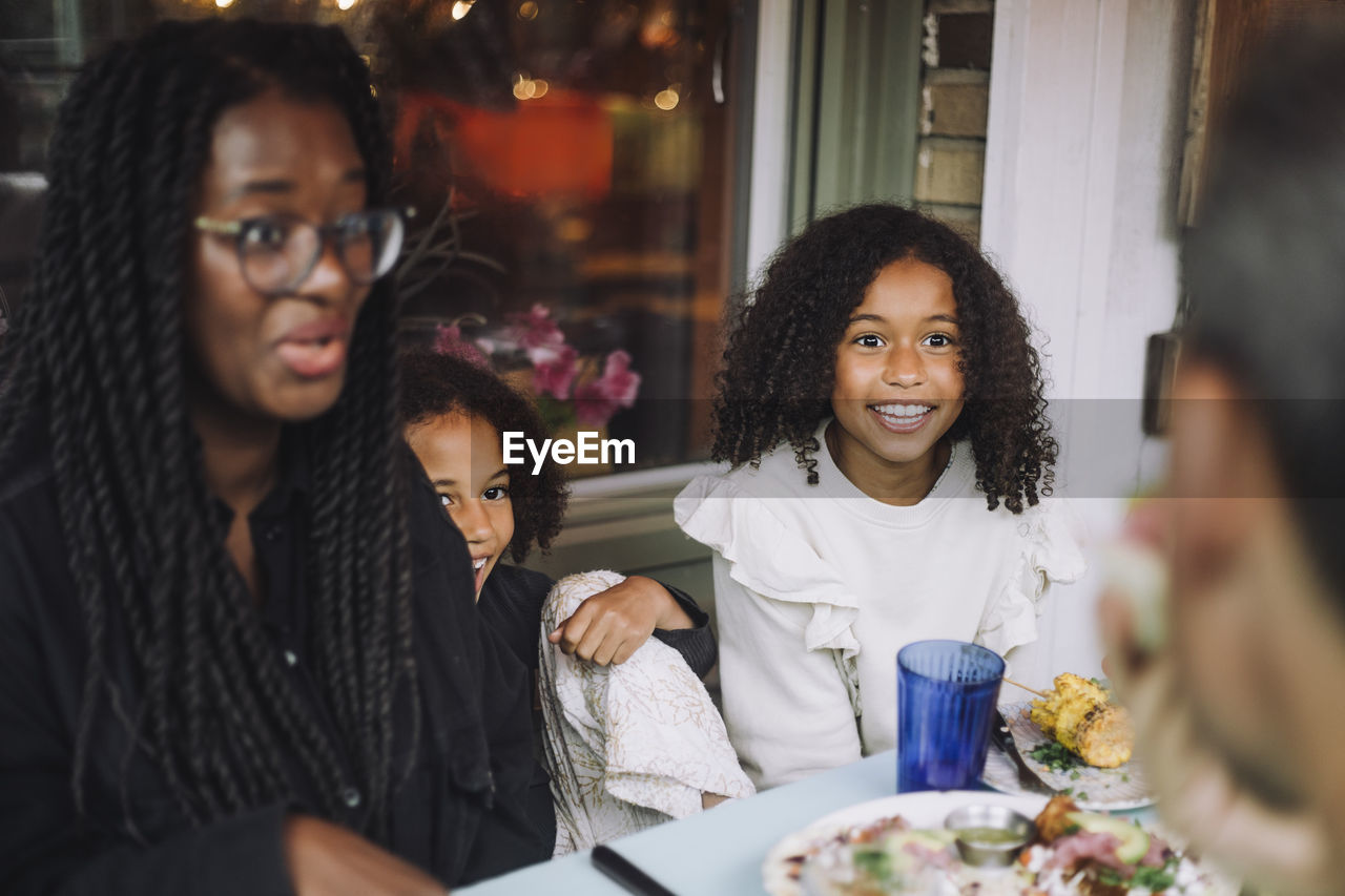 Curious sisters sitting with mother while having food at restaurant