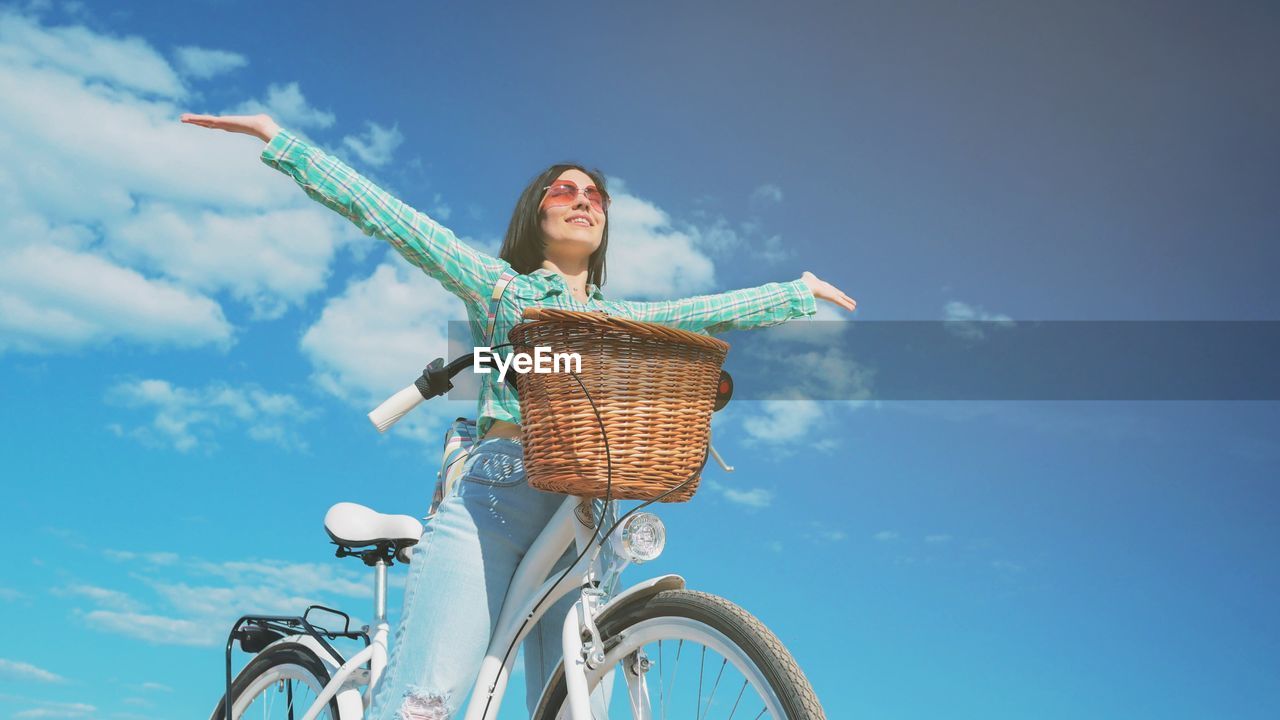 Low angle view of young woman with bicycle against sky