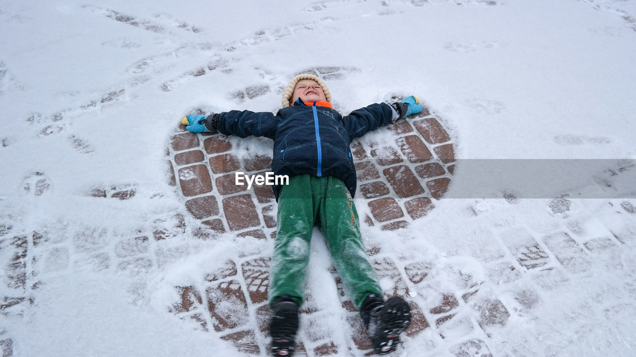 High angle view of boy lying on snowy footpath