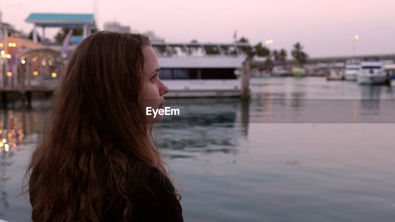 side view of woman looking at river against sky during sunset