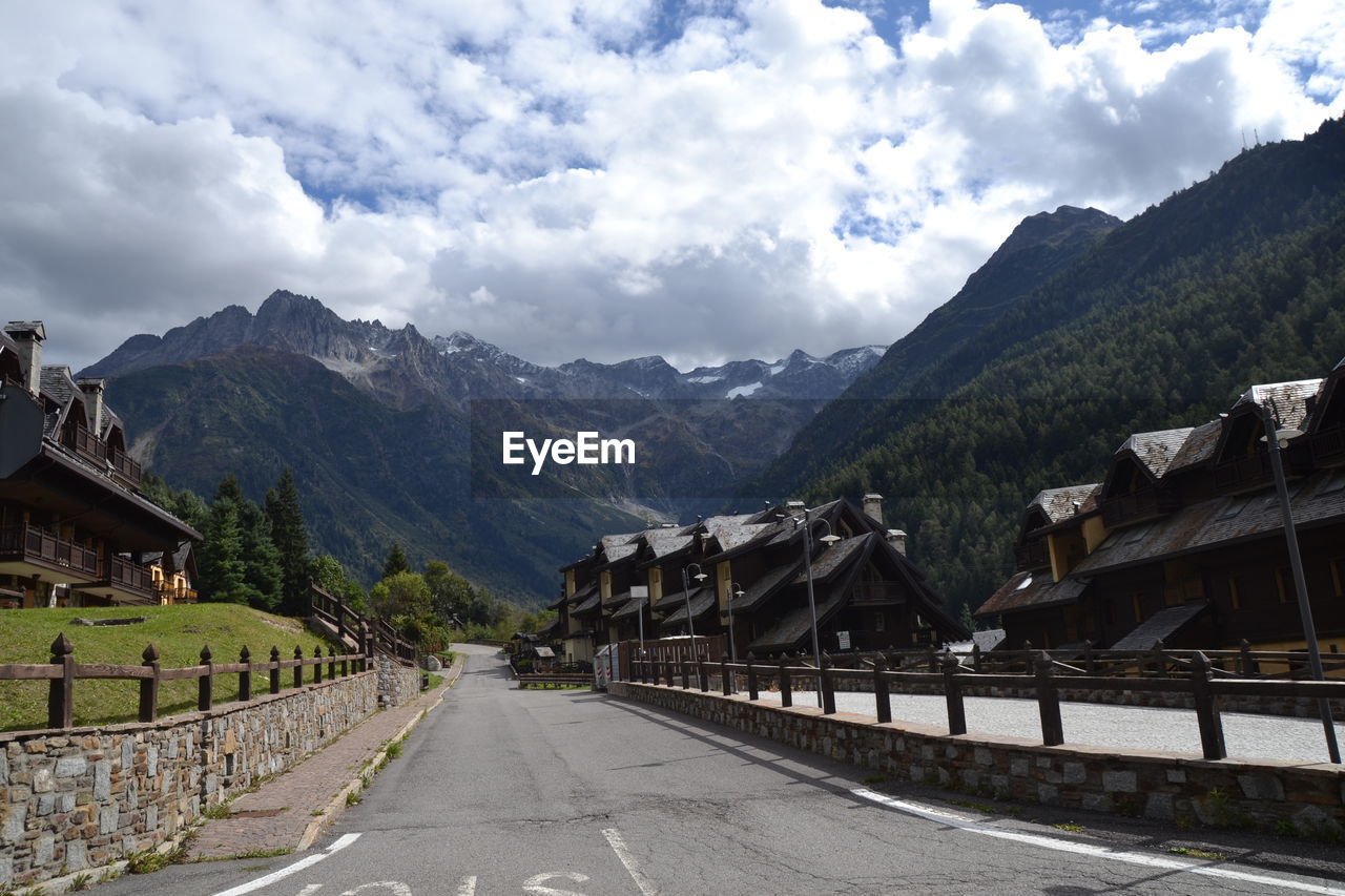 Road amidst buildings and mountains against sky