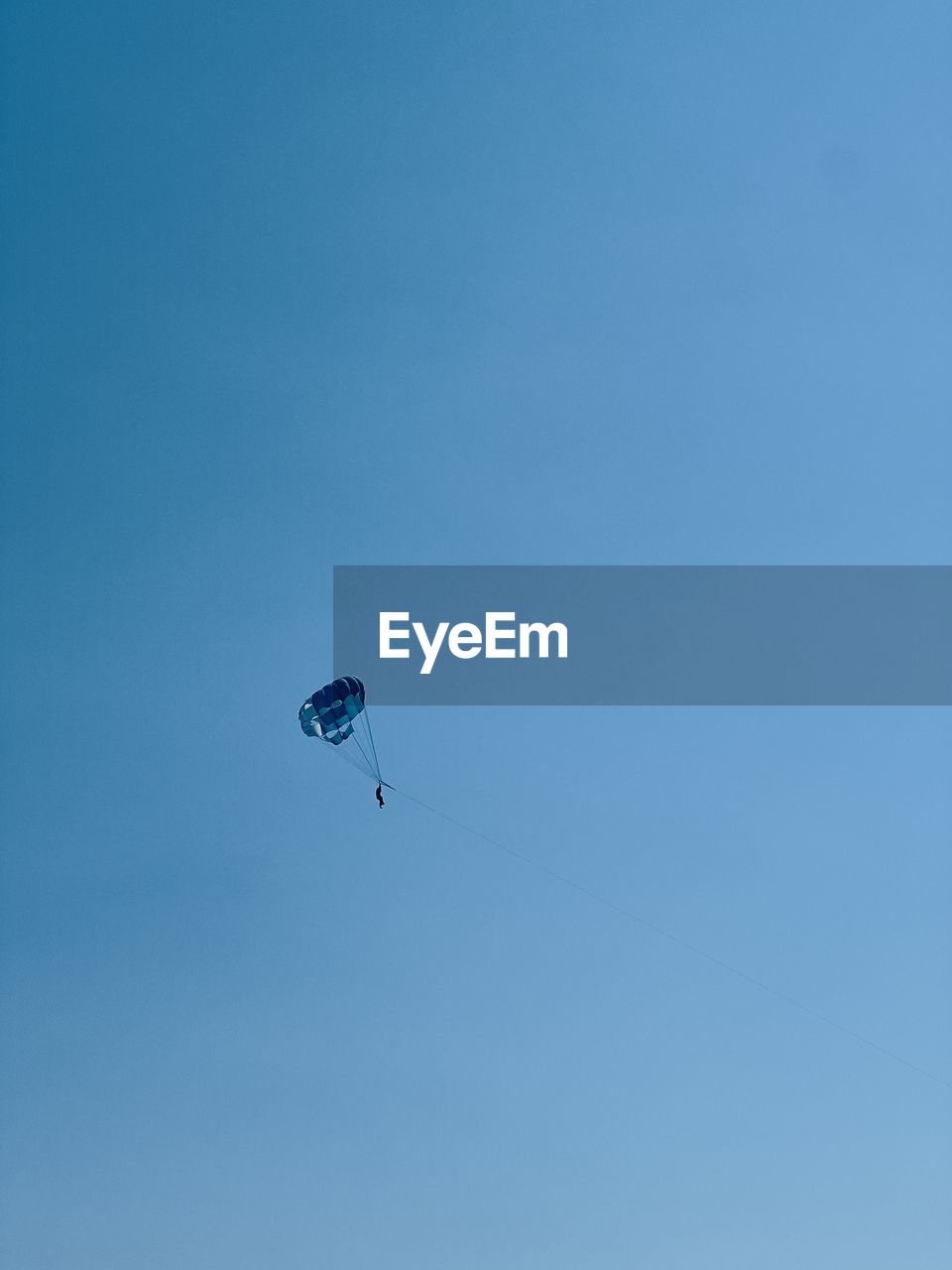 sky, blue, extreme sports, flying, adventure, mid-air, paragliding, low angle view, parachute, sports, clear sky, nature, leisure activity, windsports, day, transportation, copy space, parachuting, joy, outdoors, distant, exhilaration, motion, one person, gliding, sunny, parasailing, recreation, environment
