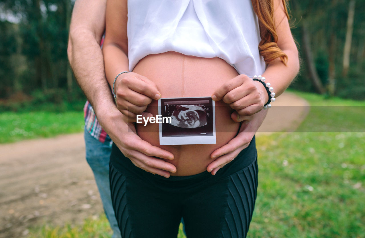 Female pregnant showing ultrasound scan of baby while her partner holding her belly