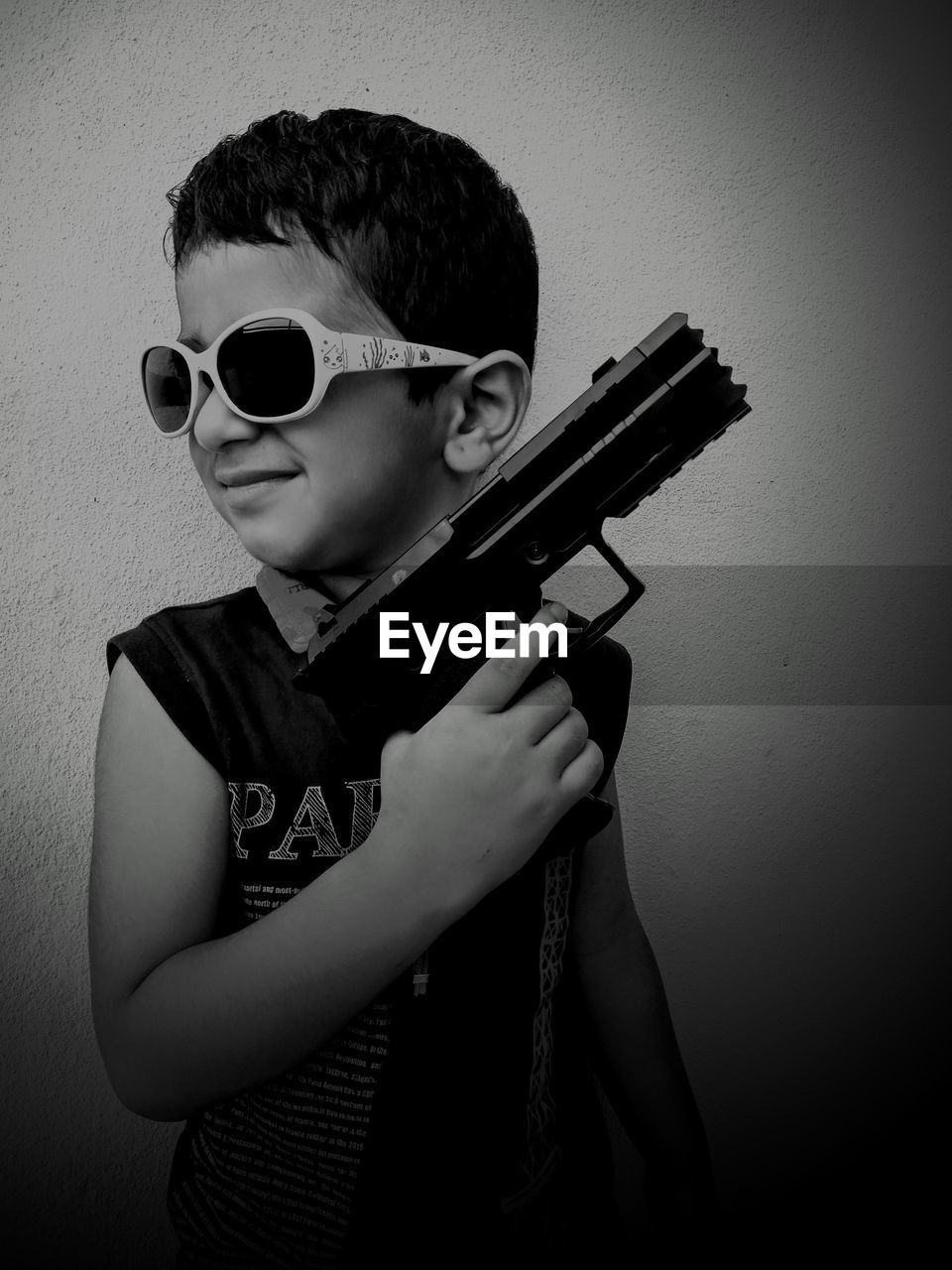 Close-up of boy wearing sunglasses while holding toy gun against wall