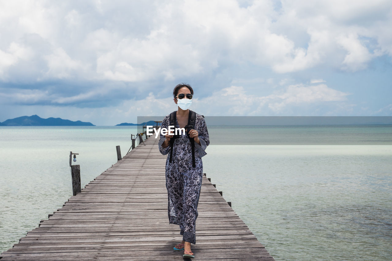 Woman in protective  mask standing on pier over sea against sky