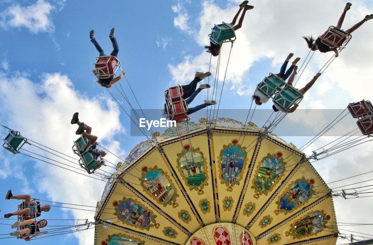 Low angle view of people sitting carousel against sky