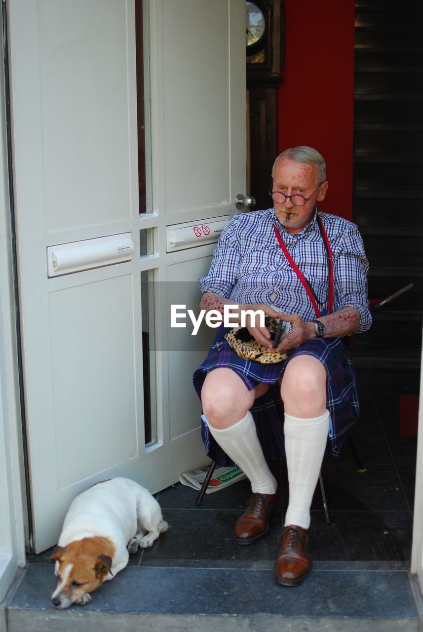 Portrait of an old man with glasses and a dog. he has scars and is dressed with style. 