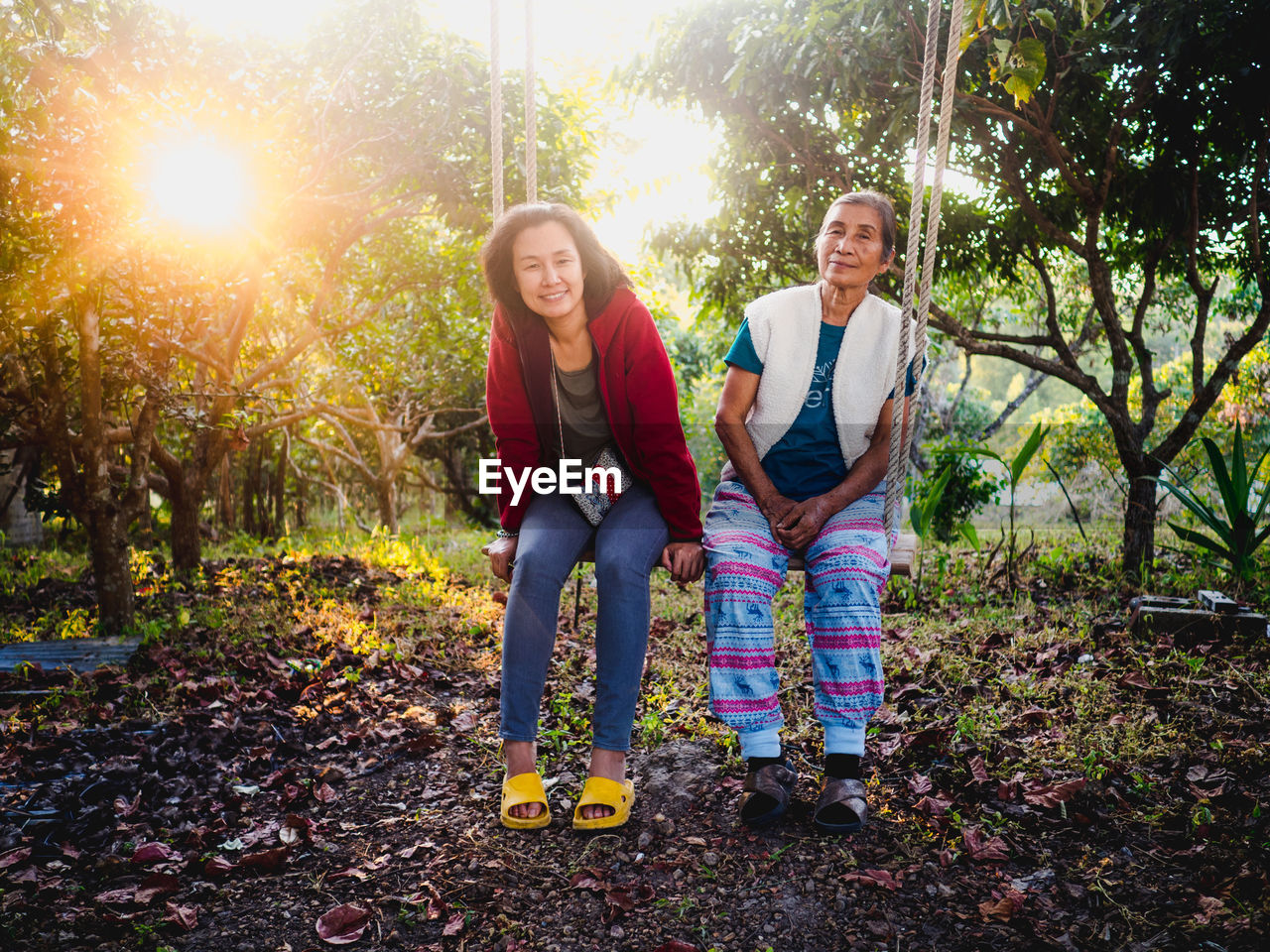 Portrait of smiling woman with mother sitting on swing against plants