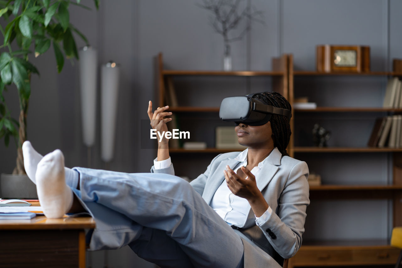 Relaxed afro woman in vr headset meditating in virtual reality at workplace during work break