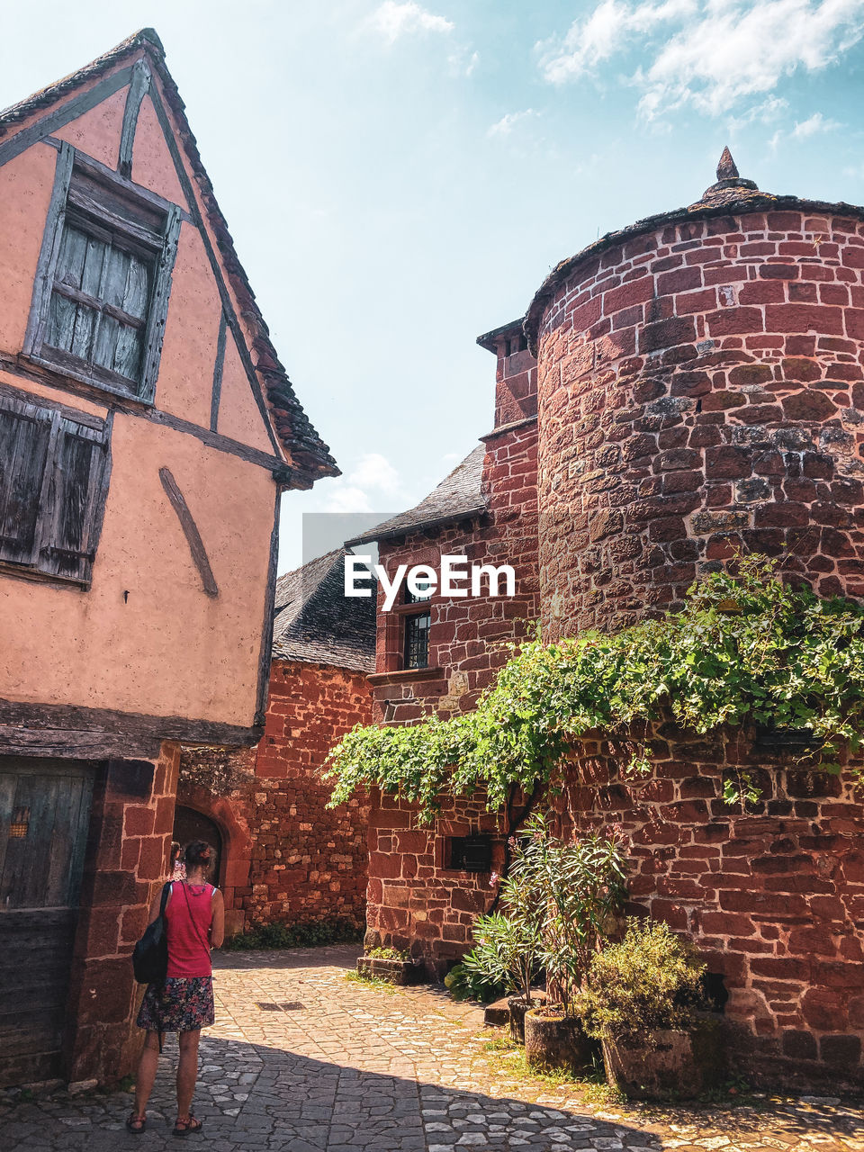 architecture, building exterior, built structure, building, wall, town, one person, house, nature, sky, brick, adult, full length, city, village, women, lifestyles, day, brick wall, rural area, standing, rear view, outdoors, history, street, residential district, cloud, the past, urban area, plant, walking, estate