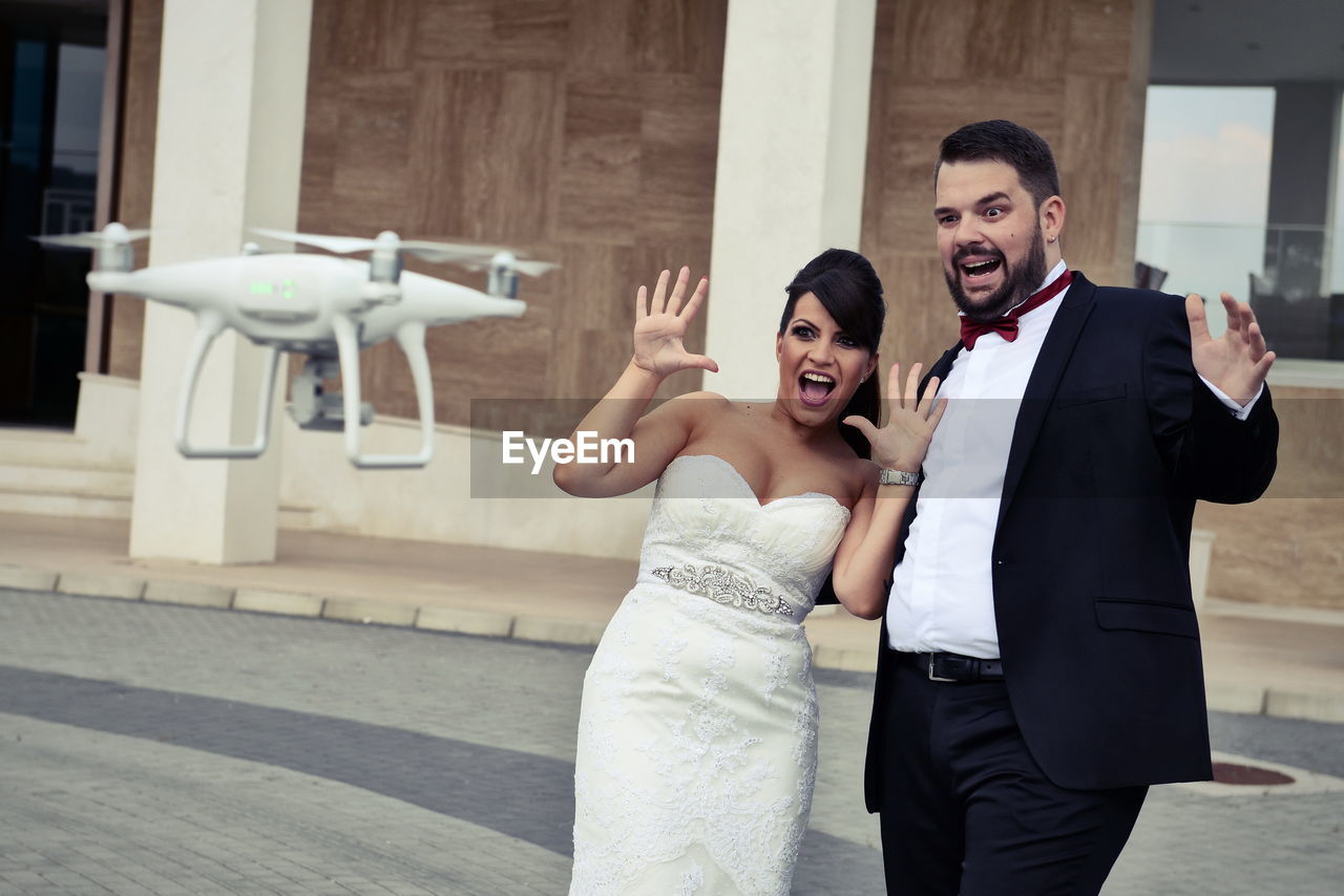 Shocked bride and groom looking at drone against building