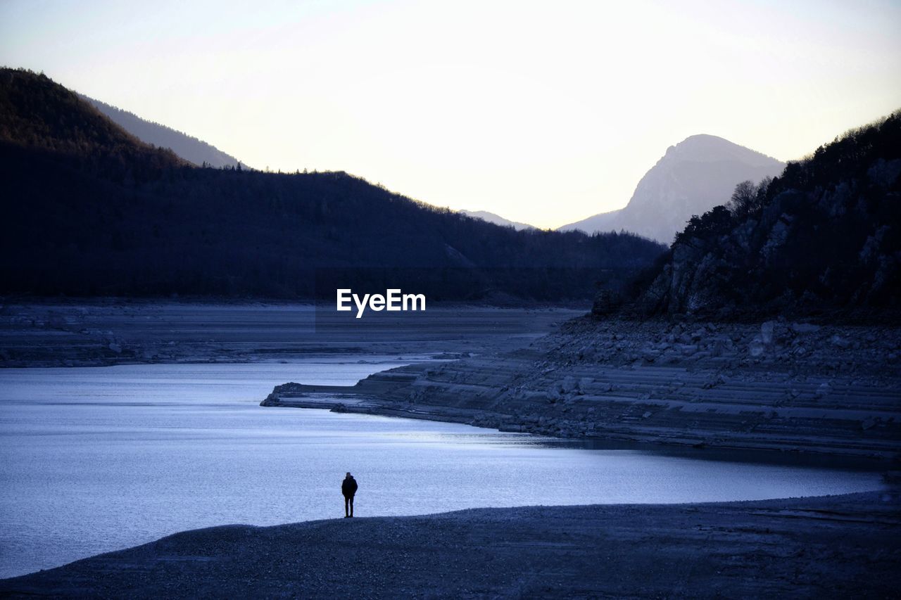 Silhouette person standing on shore against sky