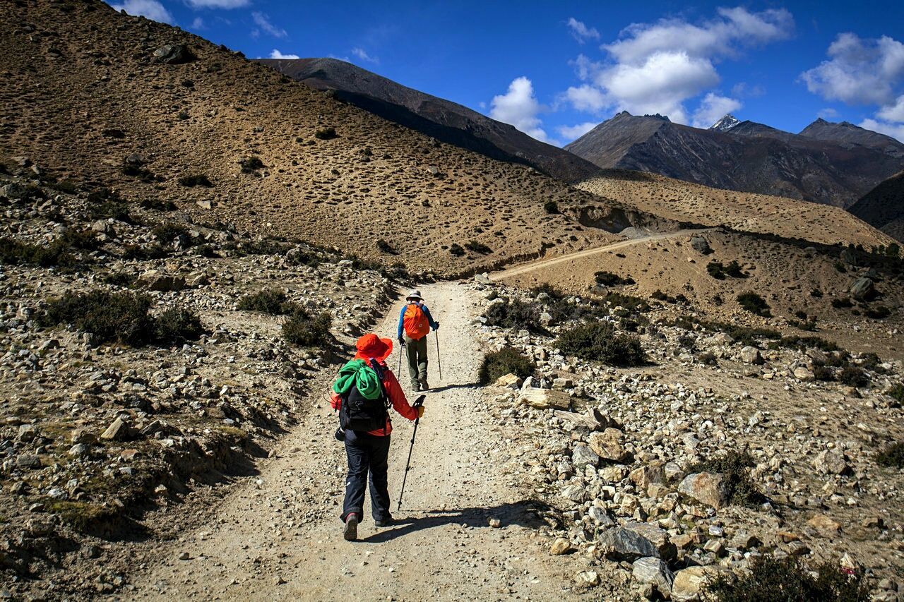 Rear view of people hiking towards mountain against sky