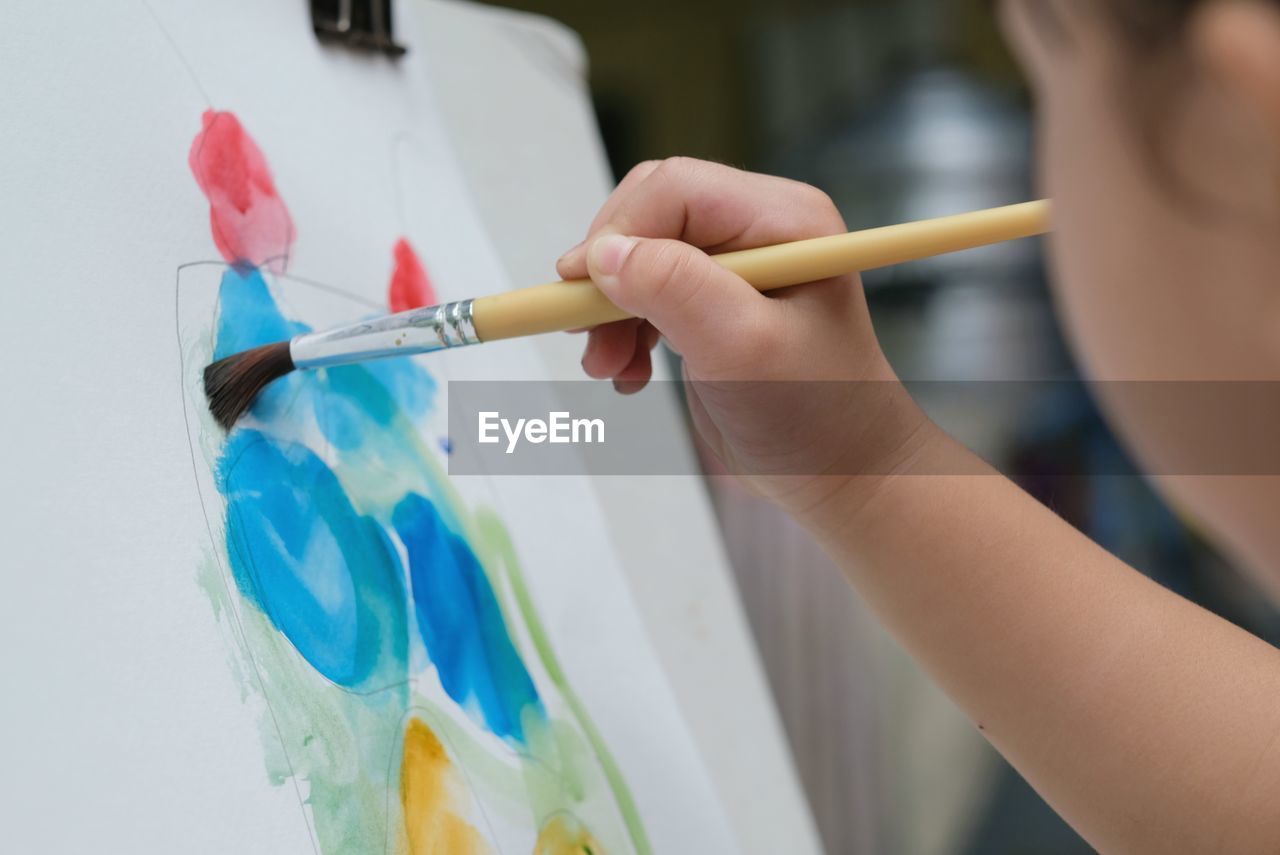 Cute asian child girl is holding paintbrush and painting on the paper. selective focus