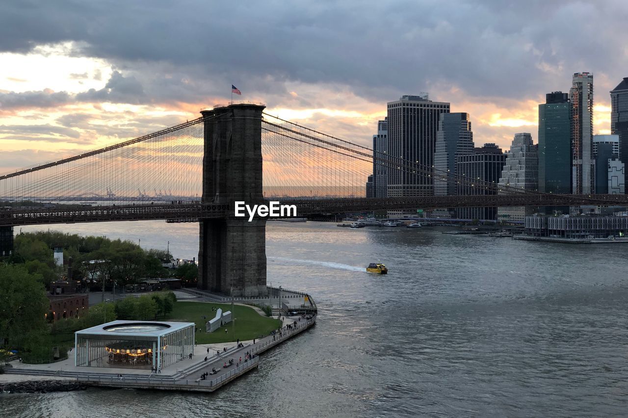 Bridge over river in city against sky during sunset