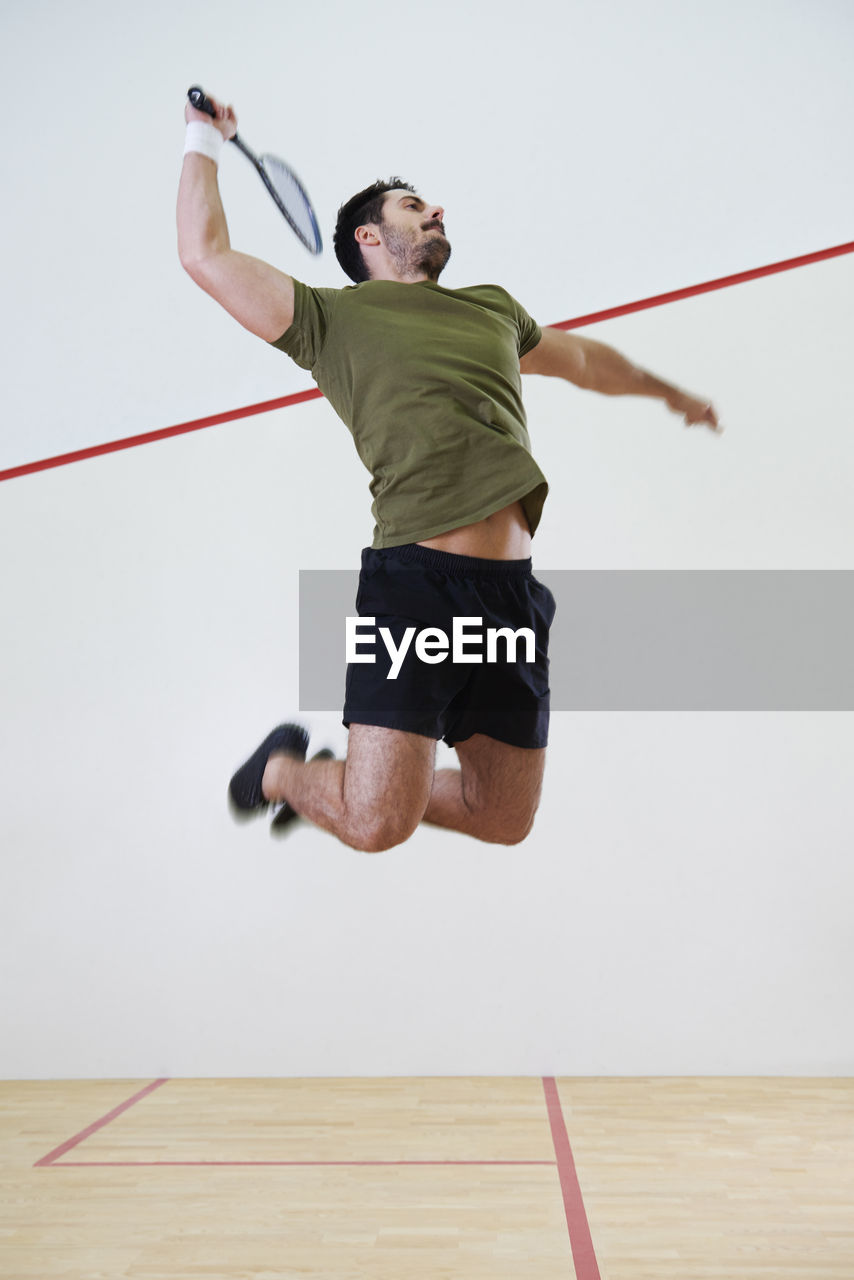 Full length of man with racket jumping on court