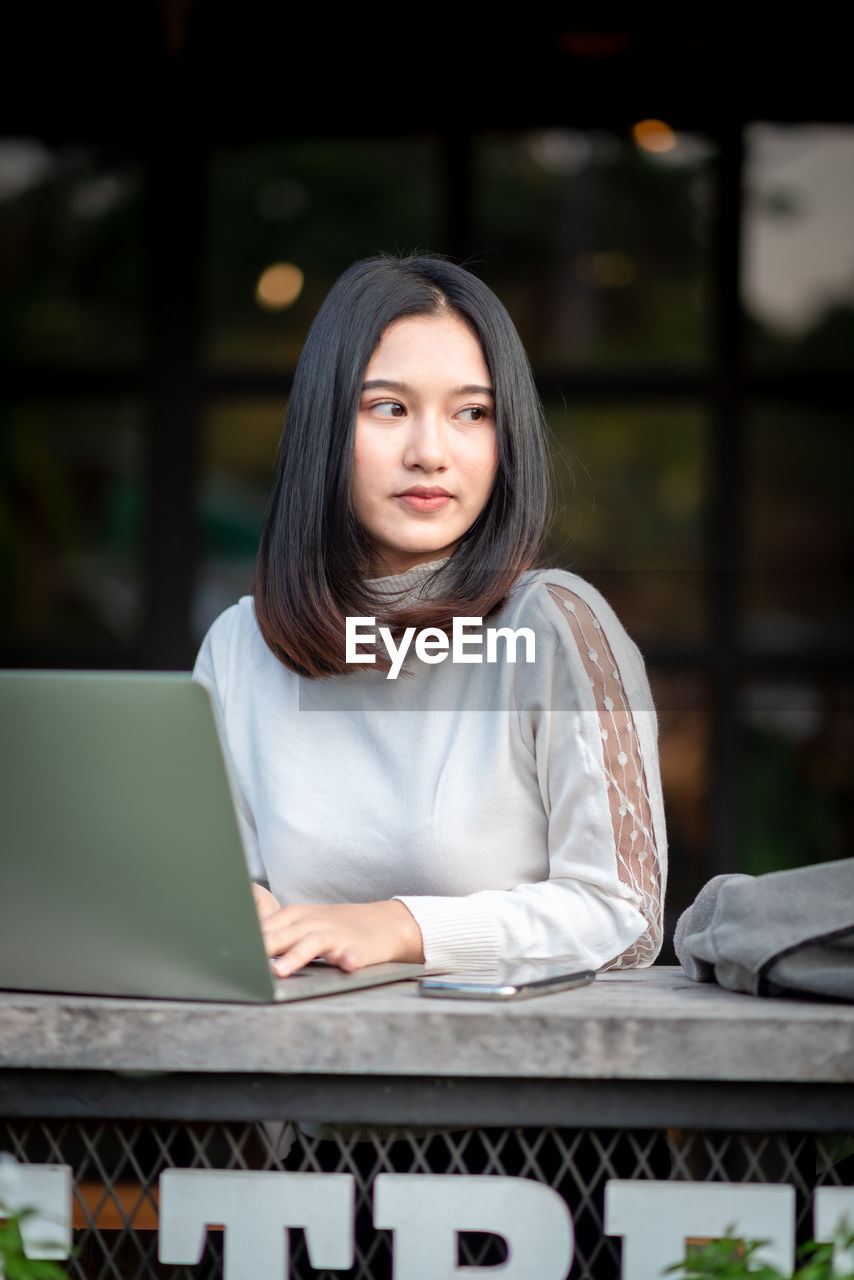 PORTRAIT OF A SMILING YOUNG WOMAN WITH LAPTOP