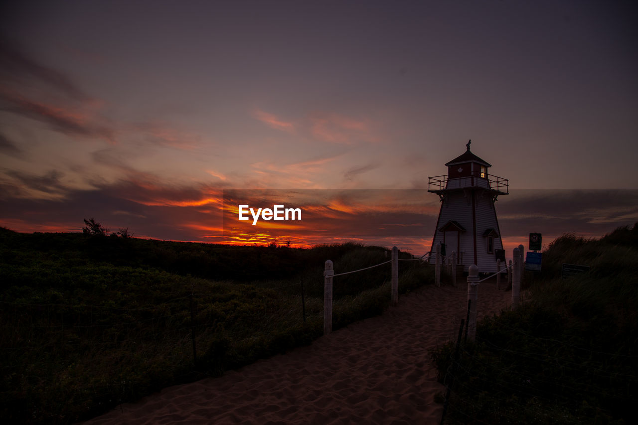 Lighthouse at beach against sky during sunset