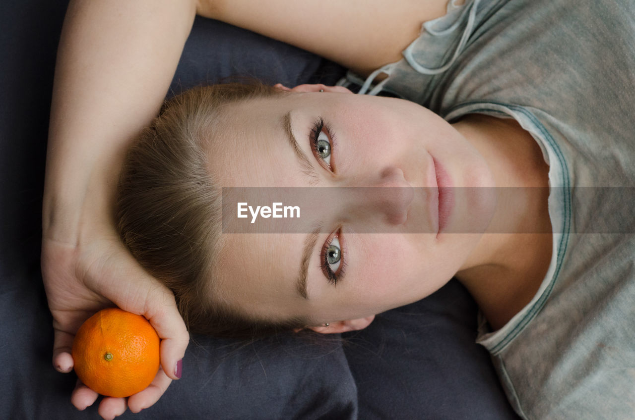 Directly above portrait of woman lying with orange fruit on bed