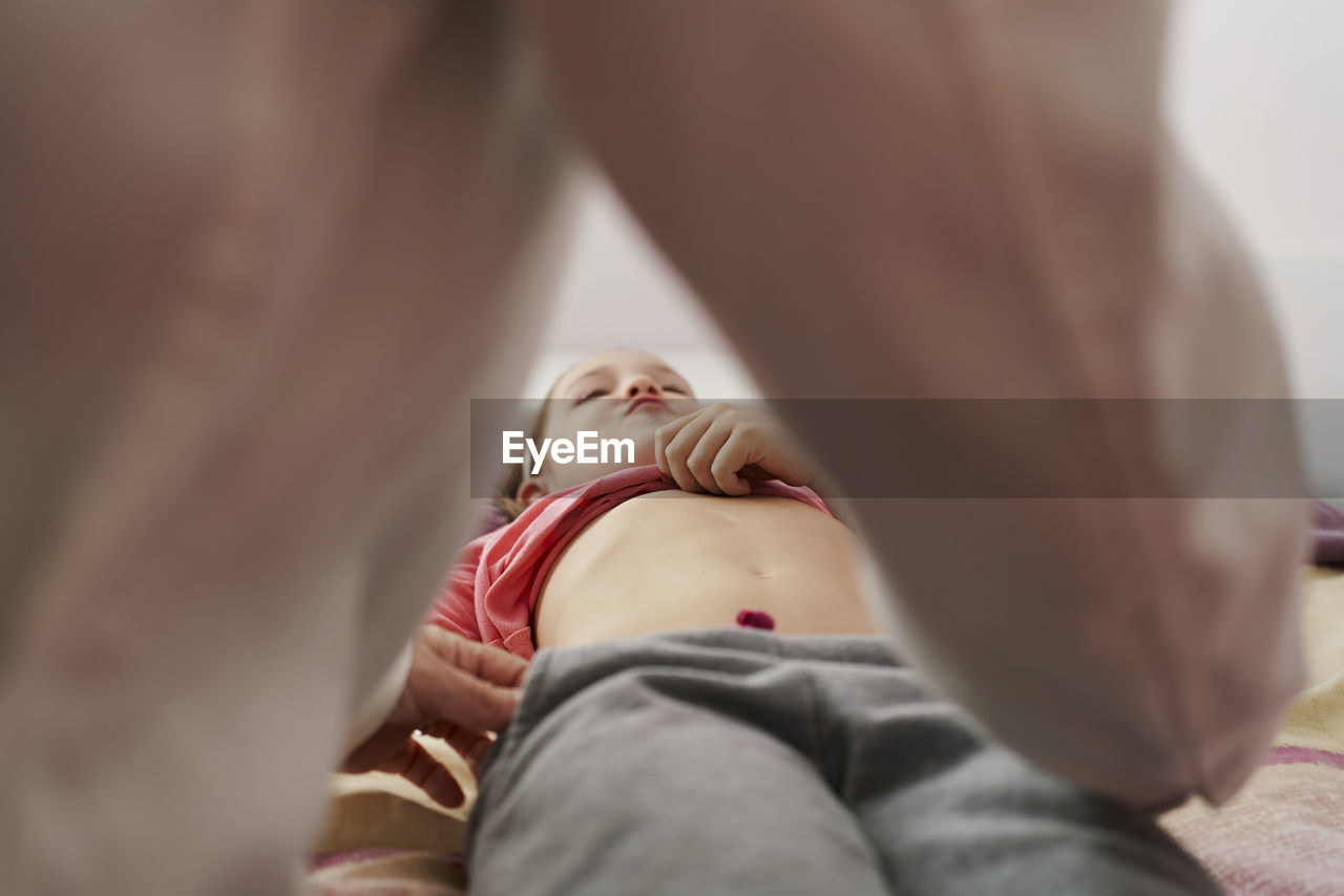 Female doctor examining a little girl's abdomen in her room. home doctor concept