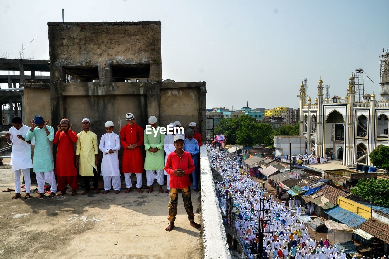 REAR VIEW OF PEOPLE STANDING AGAINST BUILDING