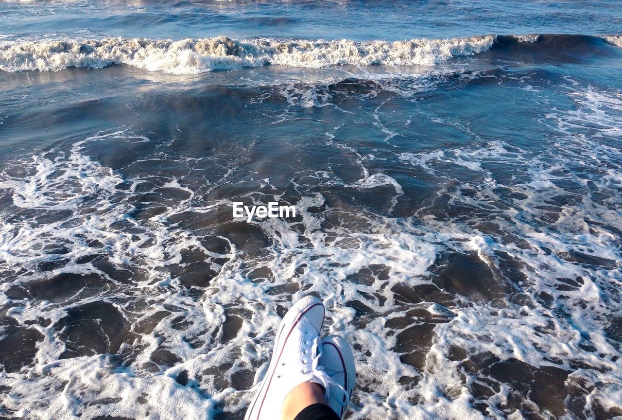 Low section of woman wearing shoes against sea