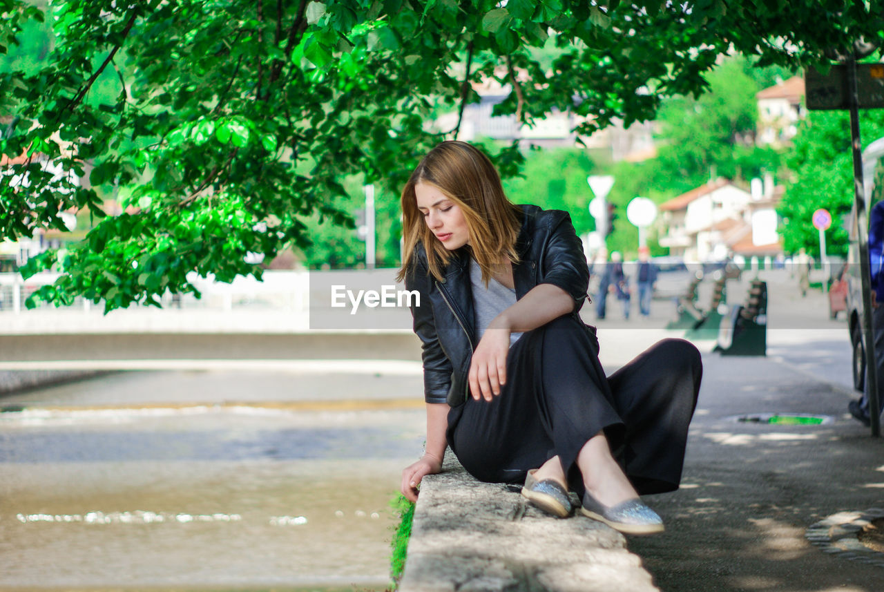 Full length of young woman relaxing on retaining wall