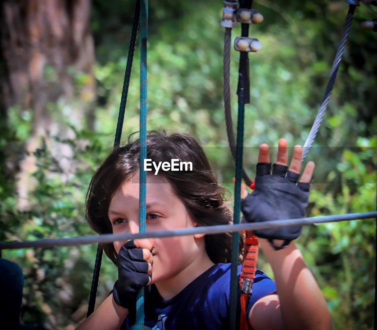 Thoughtful boy holding ropes against plants