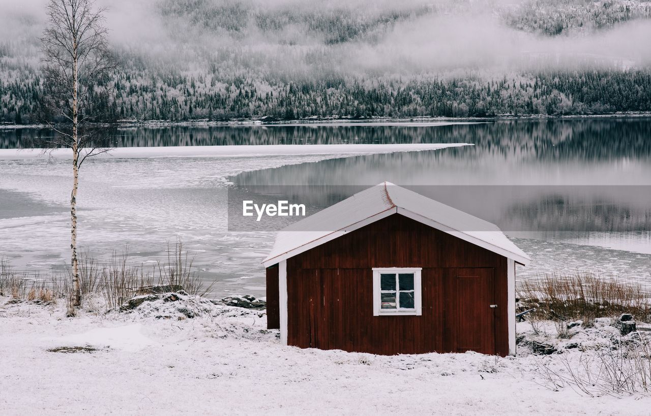 Traditional red cabin overlooking a snow covered lake and forest