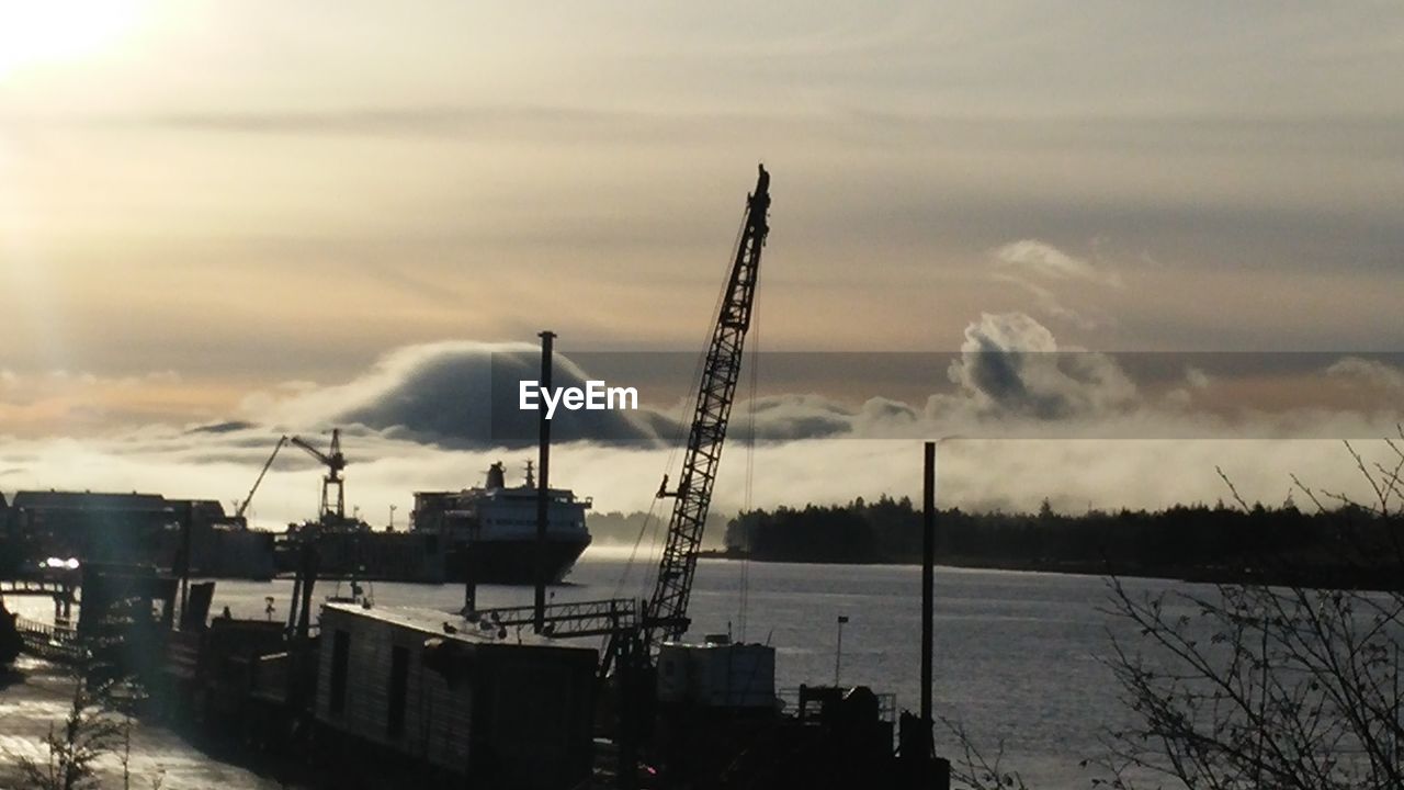 High angle view of crane at harbor on sea against sky during sunset