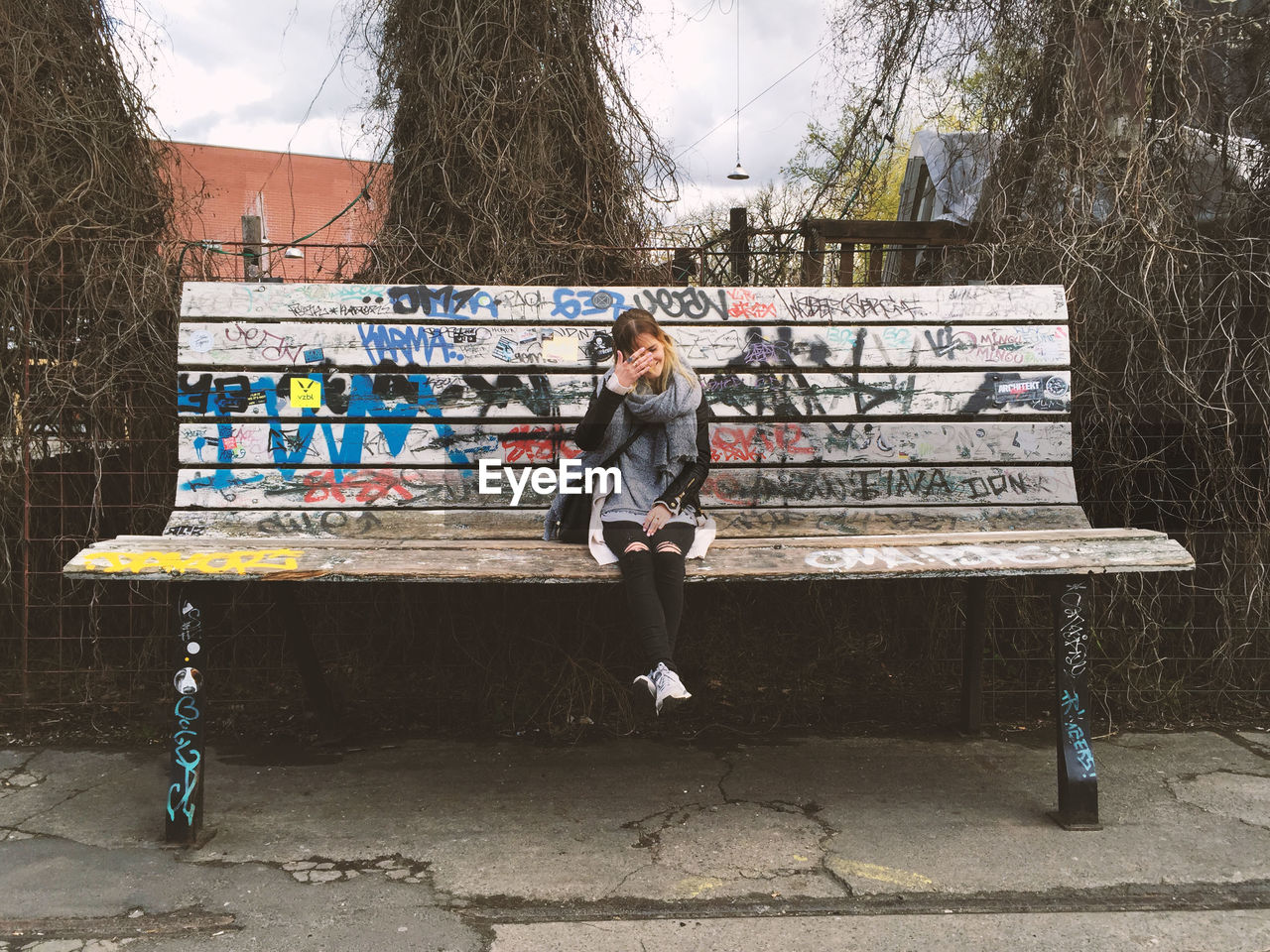 Smiling woman sitting on huge bench against fence at park