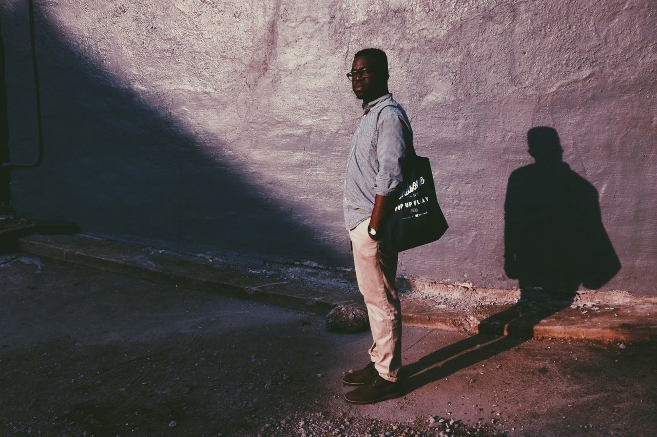 Full length of man with shadow standing against wall