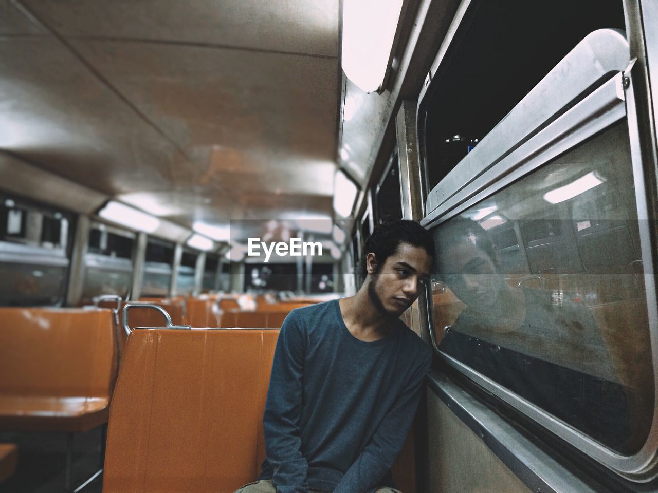 Thoughtful young man sitting by window while traveling in train