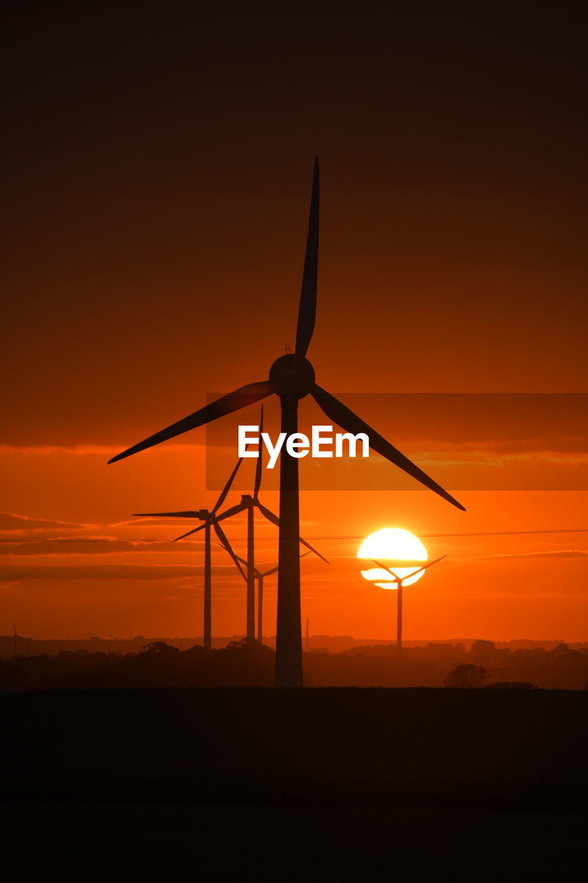 A bright red sunset through wind turbines